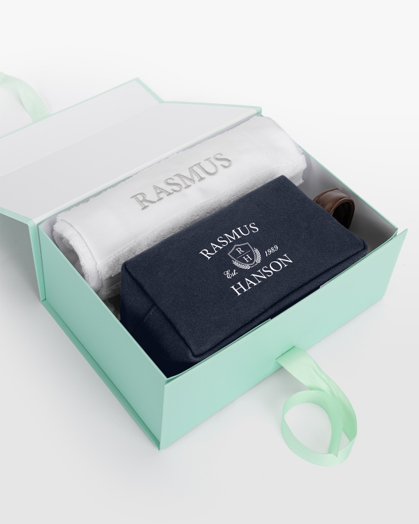 Hvitt håndklærsett (50x70) med sølvbrodert design og marineblå kanvasnecessär med navnetrykk, perfekt for stilfull komfort.