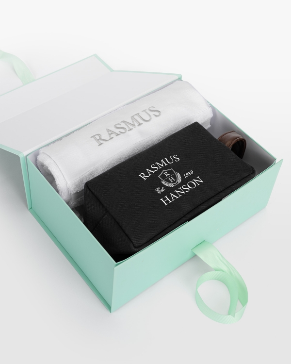 Hvitt håndklærsett (50x70) med sølvbrodert design og svart kanvasnecessär med navnetrykk, for elegant personlig stil.