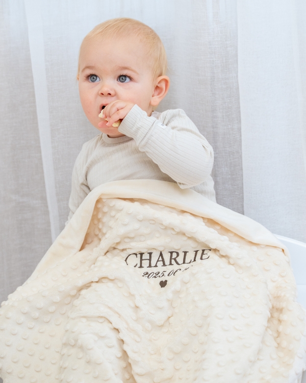 Kremfarget babyteppe med barnets navn og fødselsdato brodert på.