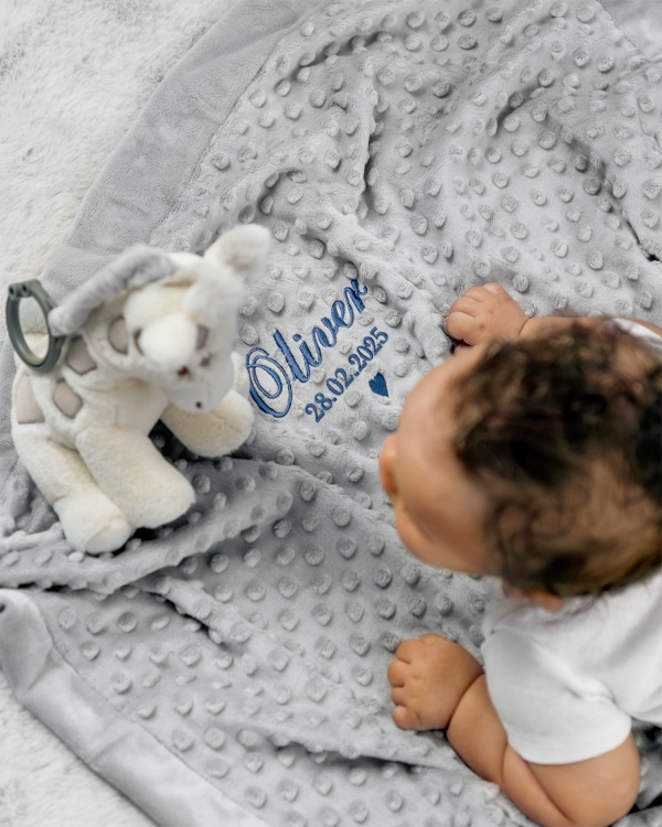 Grått babyteppe med blått broderi med navn og fødselsdato