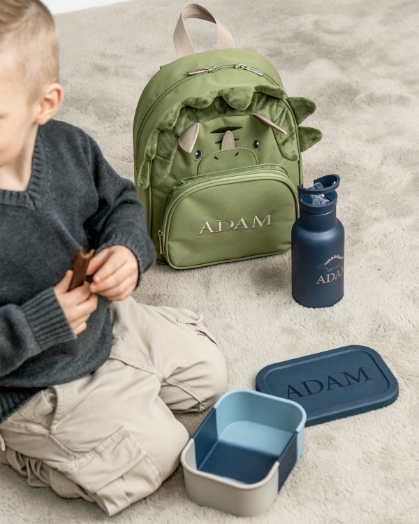 Barnesekk formet som en dinosaur, med brodert navn og blå matboks og vannflaske